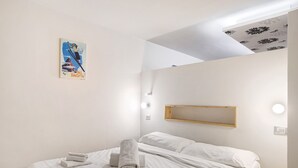 Quarto de hotel com uma cama, um cartaz na parede, um espelho e uma luminária no teto.