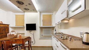 Cozinha compacta com mesa de jantar, cadeiras, televisão e chaleira.