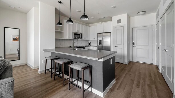 Una cocina moderna con una isla central, taburetes de bar, electrodomésticos de acero inoxidable e iluminación colgante.