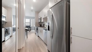 Une cuisine moderne équipée d’appareils électroménagers en acier inoxydable, un coin repas avec une table et des chaises, et une vue sur l’espace de vie.