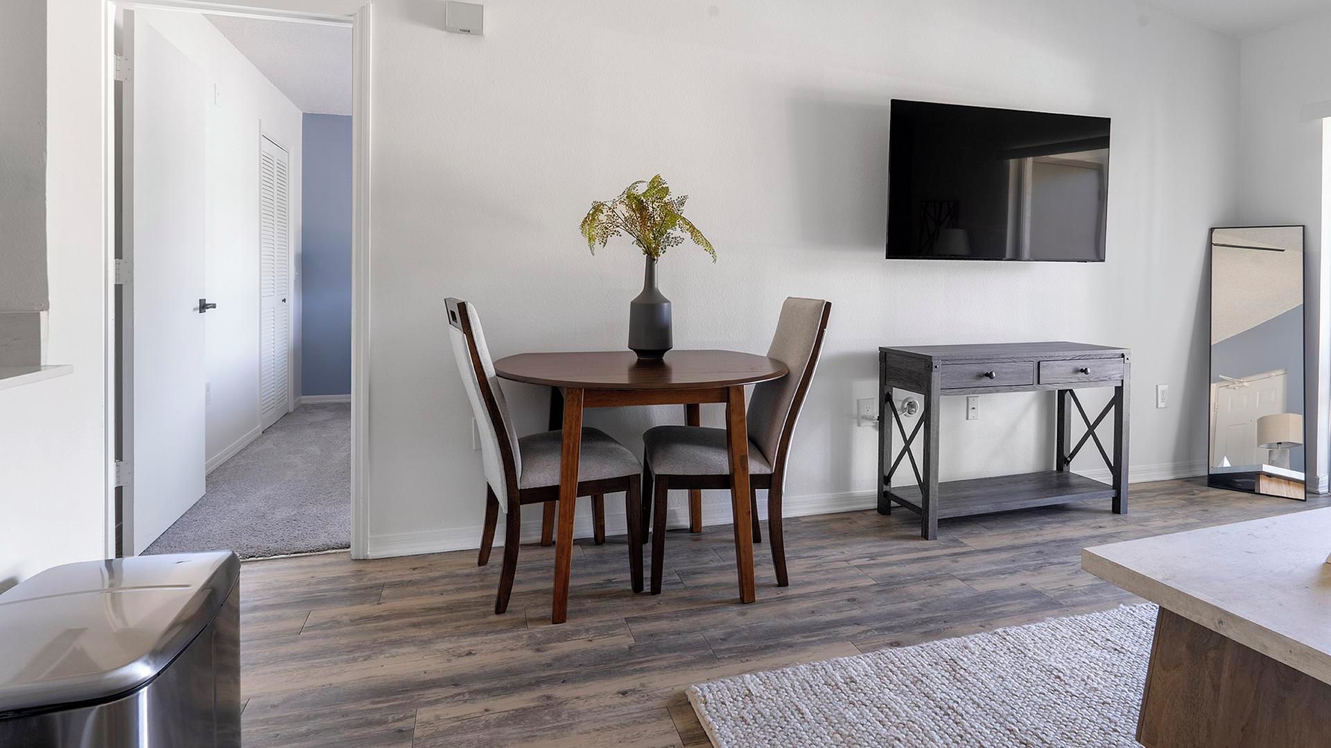 A modern living room with a dining table, chairs, a TV on the wall, and a small side table.