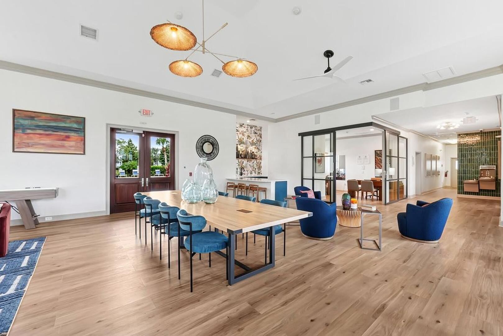 Um quarto amplo com piso de madeira, uma mesa grande com cadeiras e um ventilador de teto.