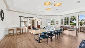 Eine geräumige Küche mit einer großen Kochinsel, moderner Pendelleuchten und großen Fenstern mit Blick ins Freie.