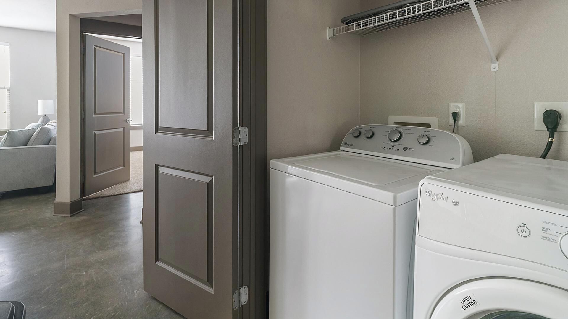 Una sala amb bugaderia, que inclou una rentadora i una destriadora, una porta i una sortida d'aire al sostre.