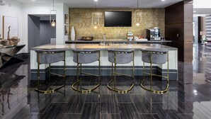A modern kitchen with a central island, bar stools, and a flat-screen TV mounted on the wall. - Landing | Beautiful 1BD, Gym (Houston)