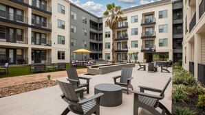 A courtyard with outdoor seating, including Adirondack chairs and tables, surrounded by multi-story buildings with balconies and large windows. - Landing | Beautiful 1BD, Gym (Houston)