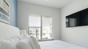 A bedroom with a bed, white pillows, a window with blinds, and a mounted TV on the wall. - Landing | Modern 1BD, Gym (Houston)