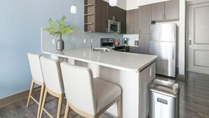 Een moderne keuken met een centraal kookeiland, barkrukken, roestvrijstalen apparatuur en een potplant.