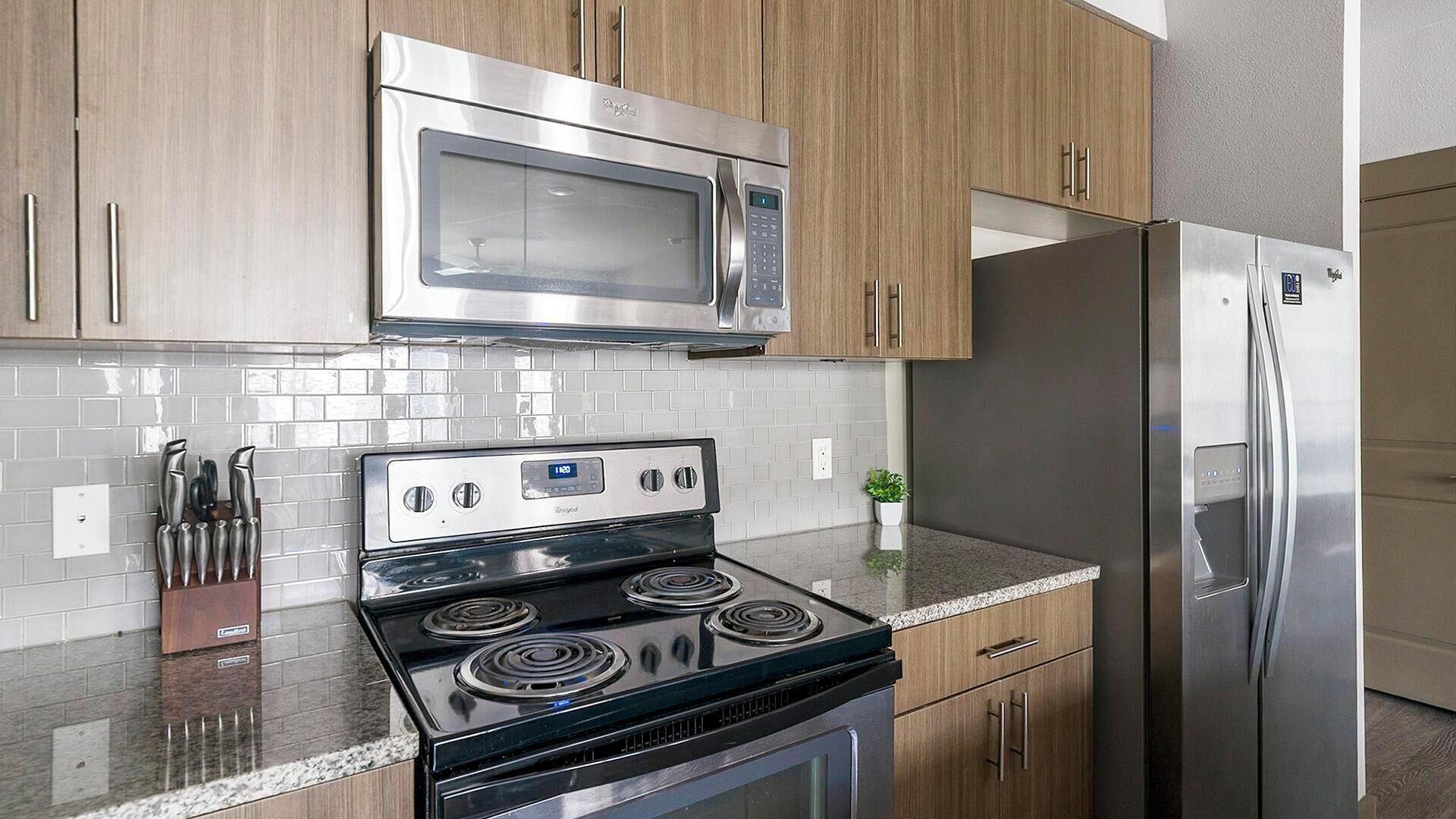 A kitchen with a stainless steel microwave, a black stove, and a refrigerator.