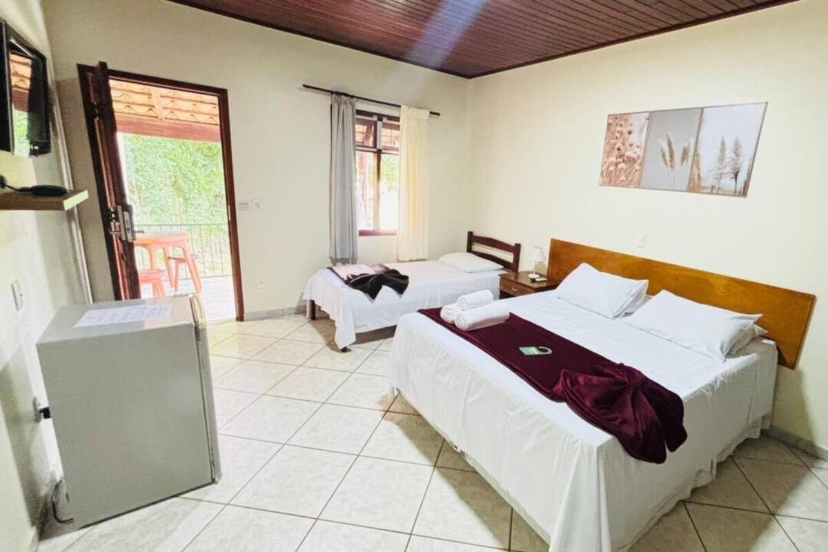 A room with two beds, a small table, a refrigerator, and a sliding door to an outdoor area.