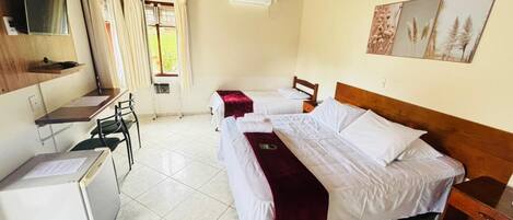 A room with two beds, a desk with a chair, a small refrigerator, and a window with curtains.