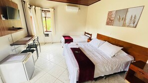 A room with two beds, a desk with a chair, a small refrigerator, and a window with curtains. - Chalés Casa Rosa (Alto Paraíso de Goiás)