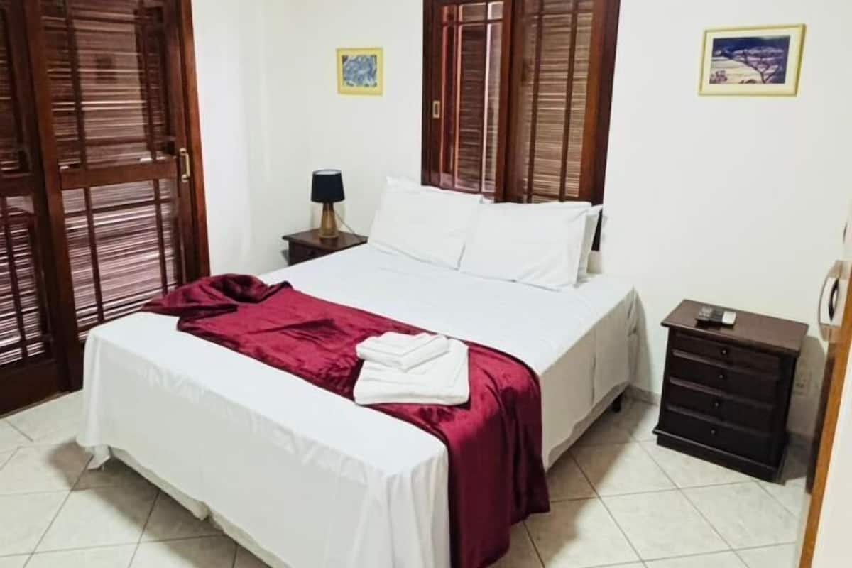 A bedroom with a bed, a nightstand, a dresser, and a window with wooden shutters.