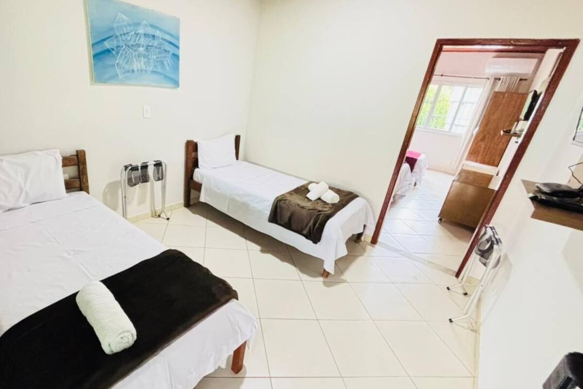 A room with two beds, a small table, a chair, a wall-mounted TV, and a door leading to another room.