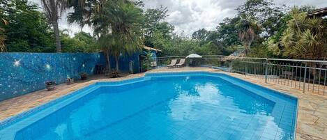 A rectangular swimming pool with clear blue water, surrounded by a stone-tiled deck.