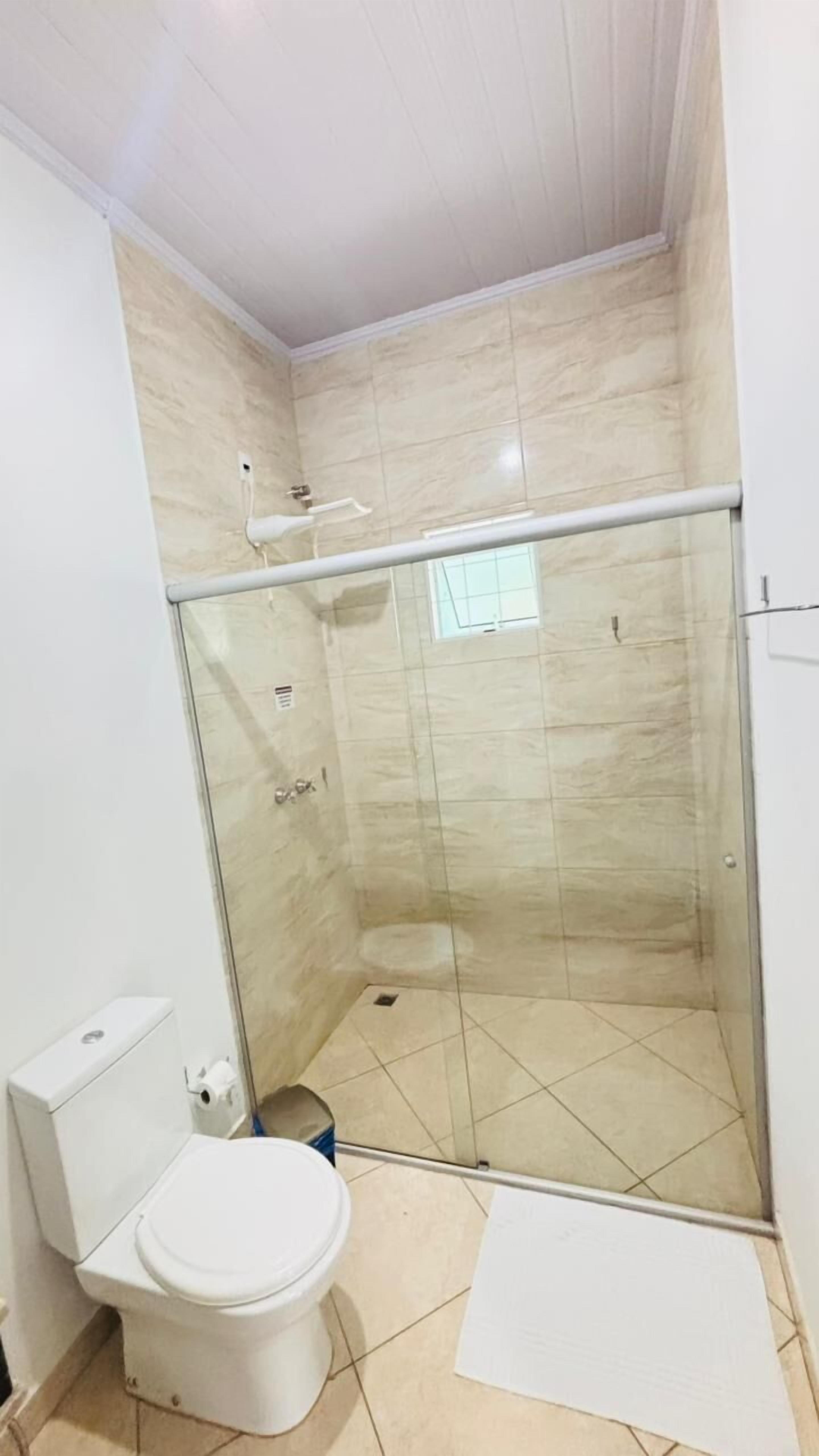 Un espacio de ducha pequeño y cerrado con puerta de vidrio, un inodoro y un tapete blanco en el suelo.