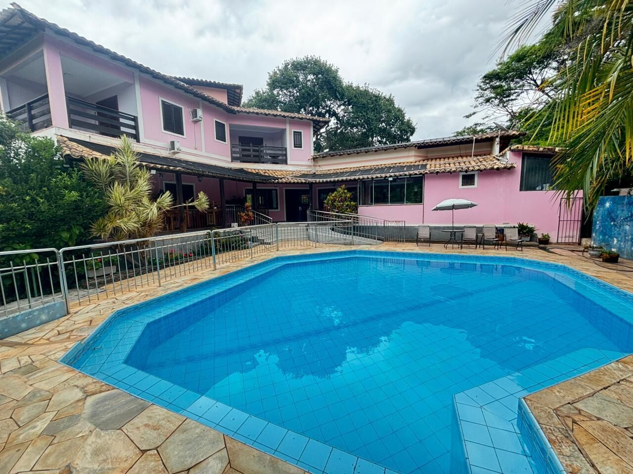 Una piscina rodeada por un edificio rosa con tejado de azulejos y suelo de piedra.