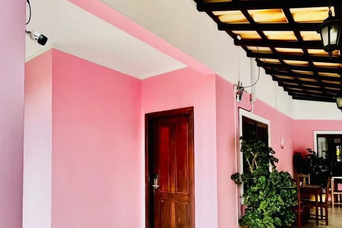A corridor with pink walls, a wooden door, and a tiled floor.