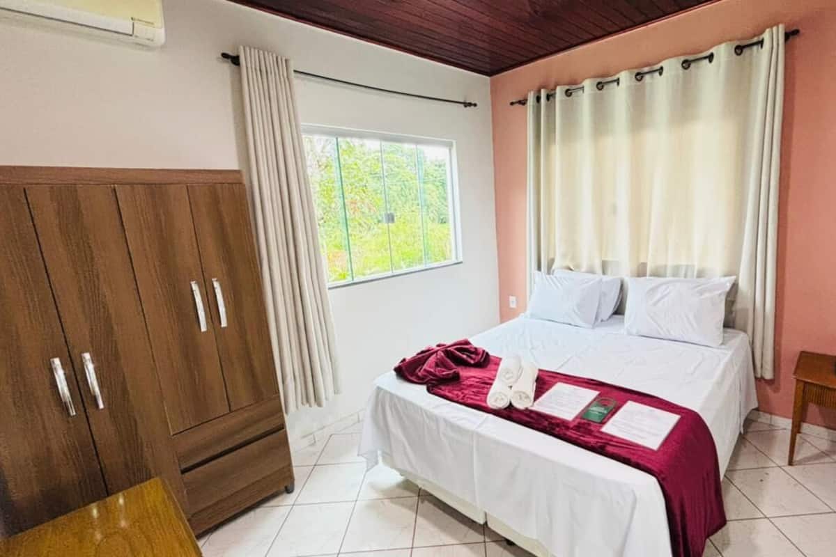 A bedroom with a bed, a wooden wardrobe, a bedside table, and a window with curtains.