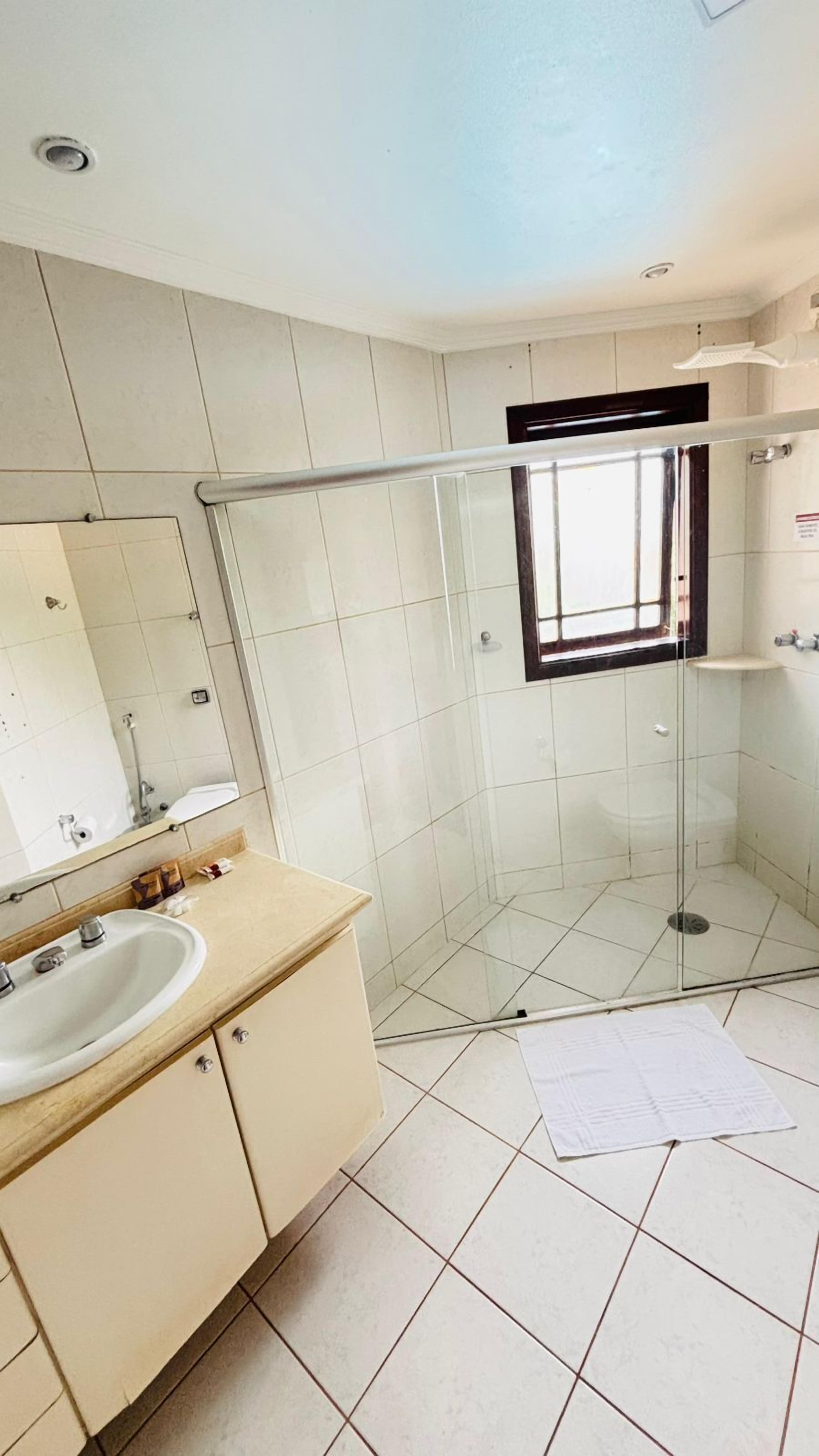 A bathroom with a glass shower enclosure, a sink with a mirror, and tiled walls.
