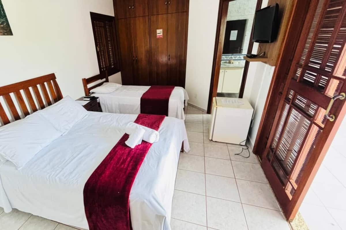 A room with two beds, a wardrobe, a television, and a small refrigerator.
