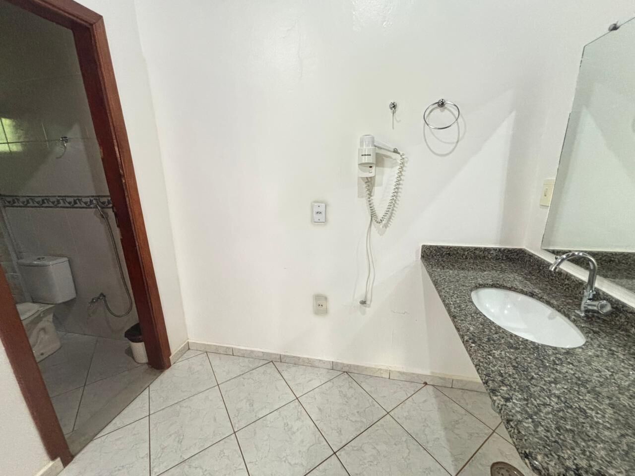 Une salle de bain avec un lavabo blanc, un miroir et une pomme de douche fixée au mur.