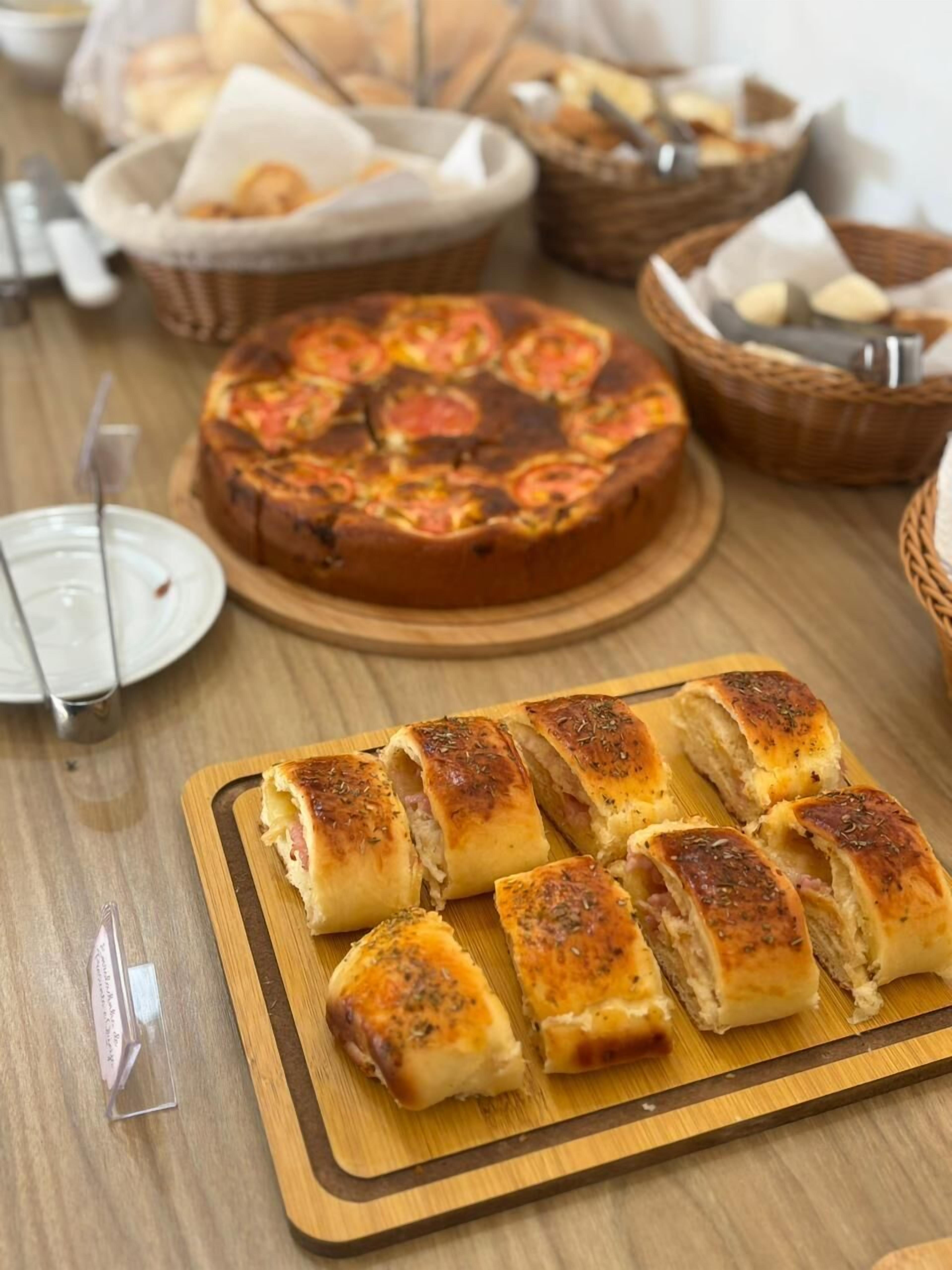 A wooden table with a pizza, bread rolls, and a bread basket.