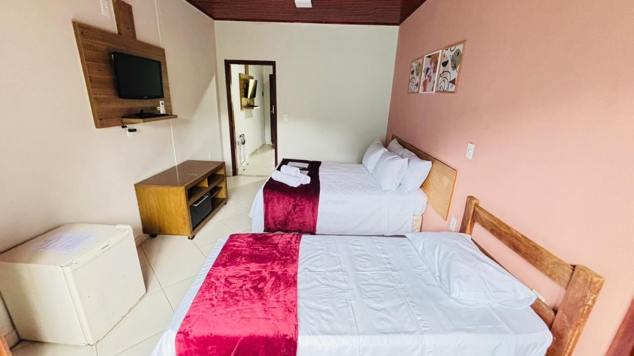 Une chambre d’hôtel avec deux lits, un téléviseur fixé au mur, une armoire en bois et un miroir.