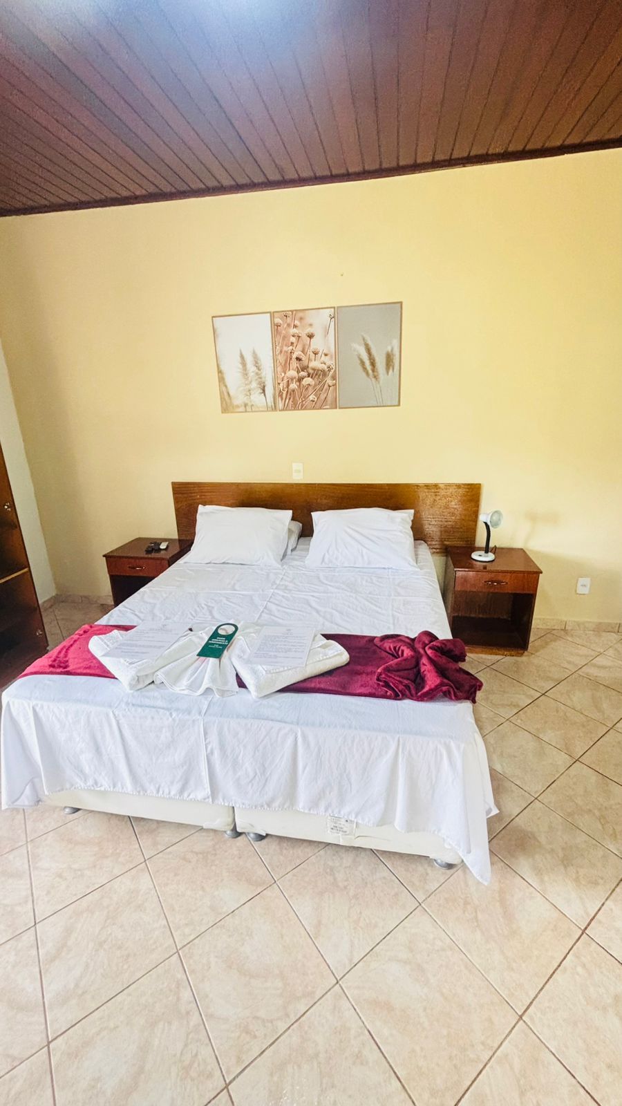 A neatly made bed with white linens, a wooden headboard, a nightstand with a lamp, and a wall-mounted picture.