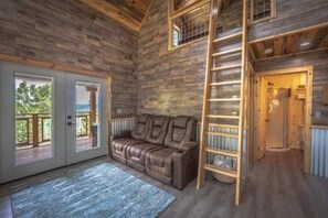 A wooden cabin interior with a sofa, a ladder, and a door leading to an outdoor deck. - RidgeWalk Treehouse - Epic Views at 9200' & Decks (Angel Fire)