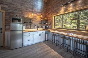 Eine Küche mit Holzwänden, einem Kühlschrank, einer Mikrowelle und einem Fenster mit Blick auf einen Wald.