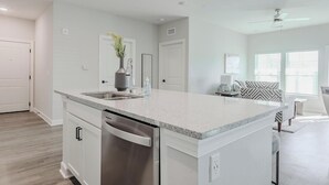 A modern kitchen with a central island, white cabinetry, and a built-in dishwasher. - Landing | Incredible 2BD, Pool (Tice)