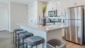 A modern kitchen with a central island, stainless steel appliances, and bar stools. - Landing | Incredible 2BD, Pool (Tice)