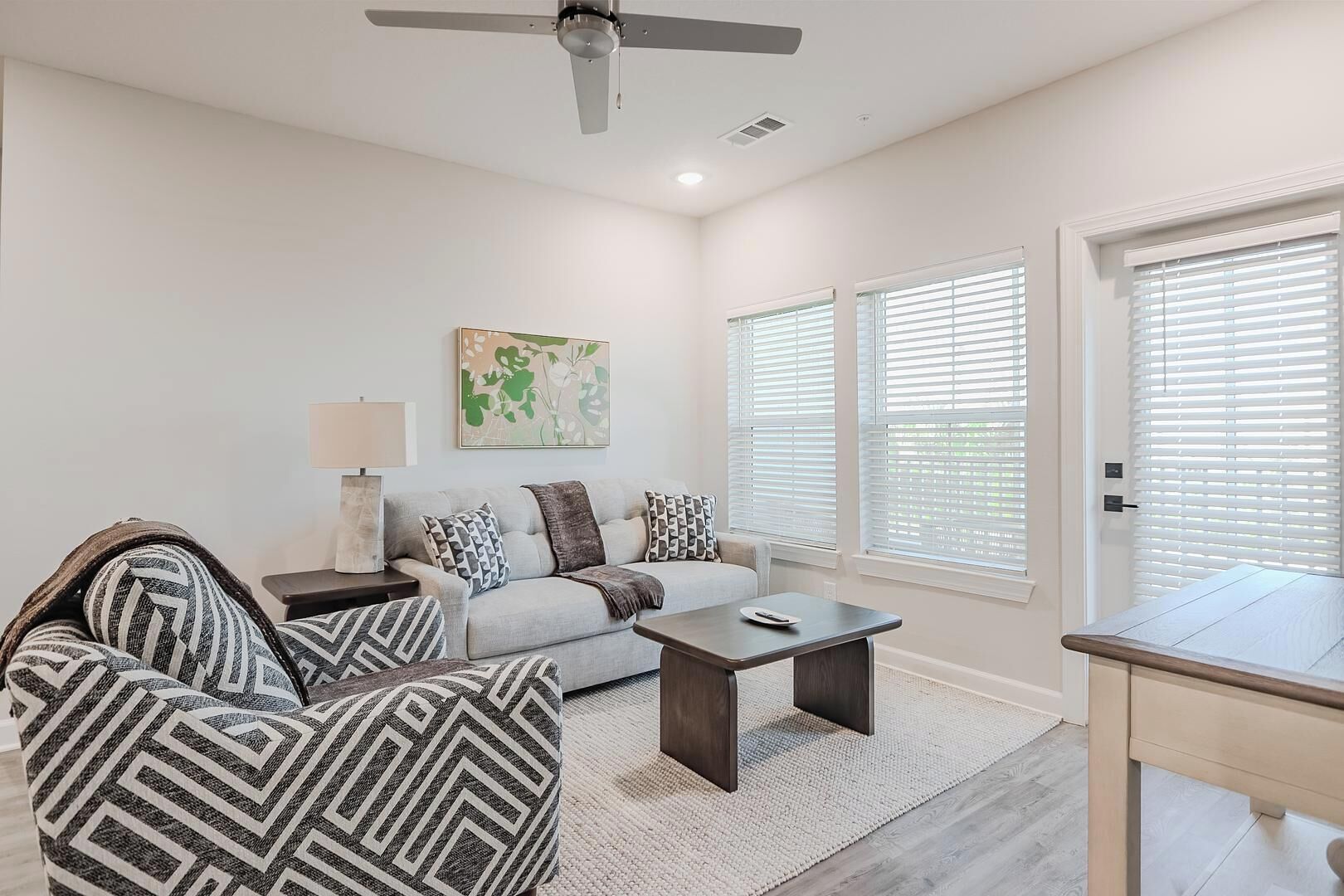 A modern living room with a sofa, armchairs, a coffee table, and a ceiling fan.