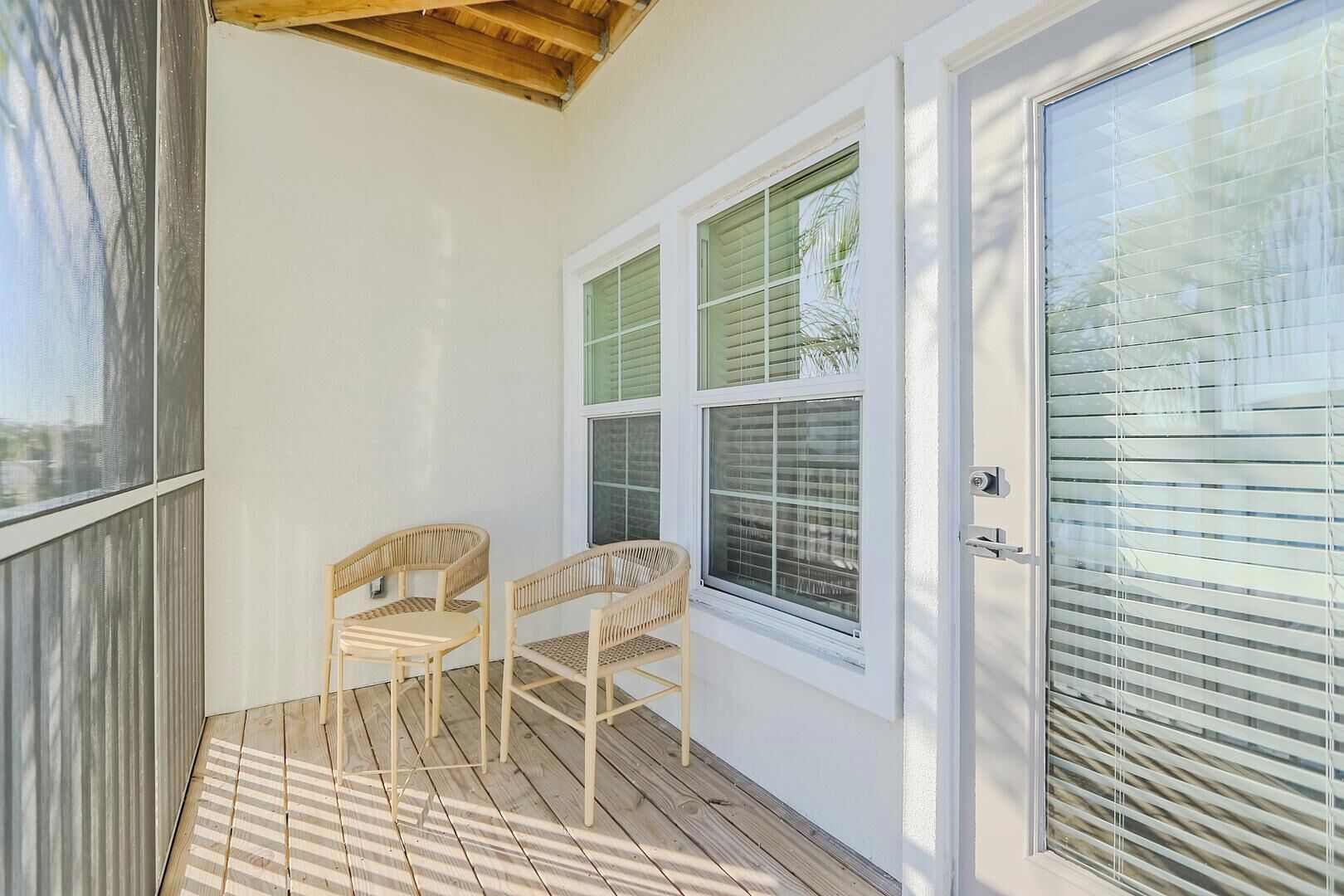 A covered patio area with two wicker chairs, a wooden ceiling, and a door with blinds.