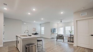 Una cocina amplia con una isla central, un comedor con mesa y sillas, y una sala de estar con sofá y televisor.