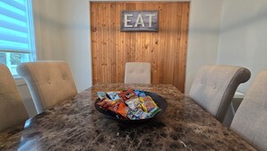 Uma mesa de jantar com uma tigela de petiscos, quatro cadeiras e uma parede de madeira com a placa 'EAT'.