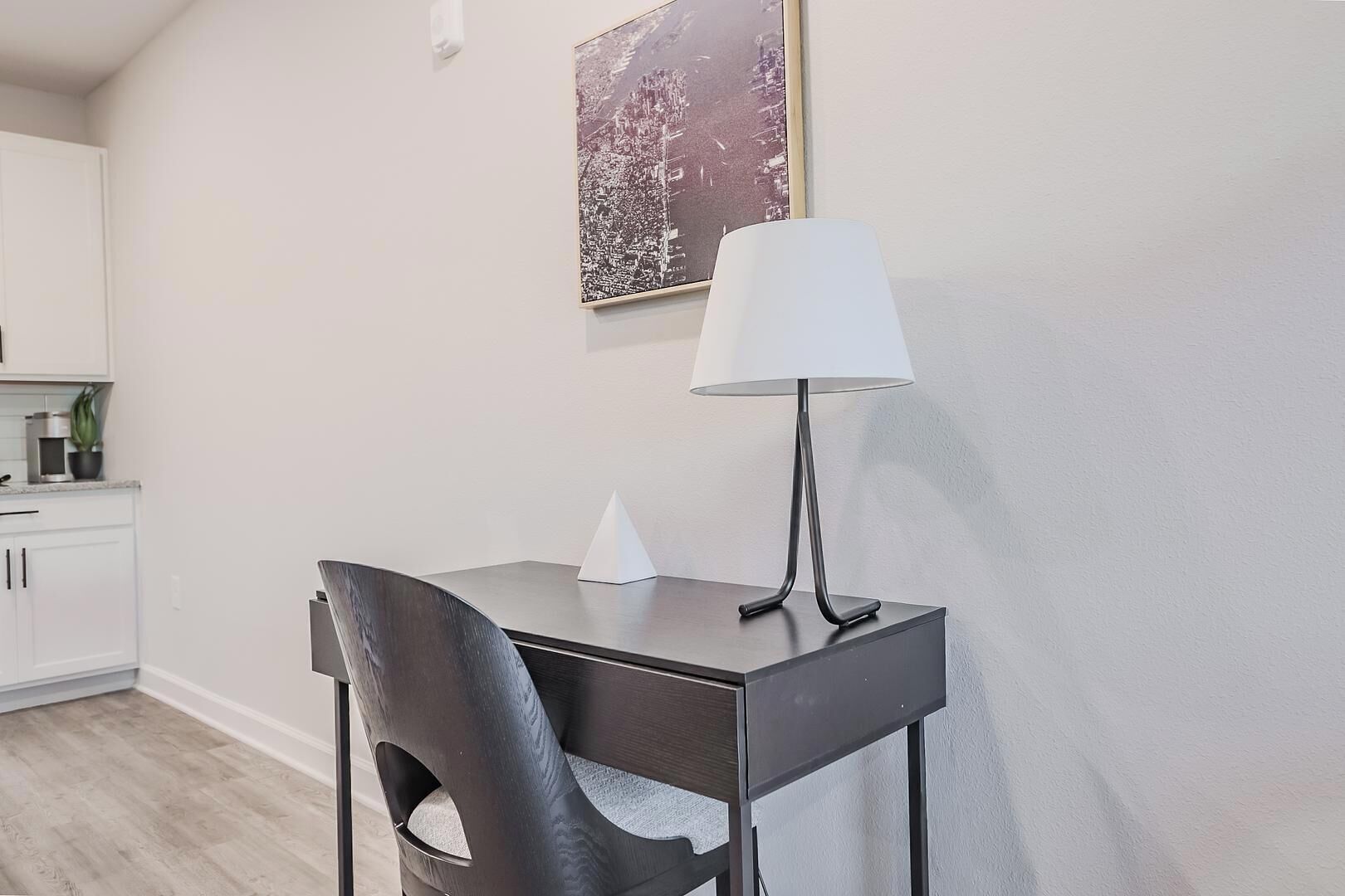 A modern kitchen with white cabinets, a dark countertop, a white lamp, and a framed picture on the wall.