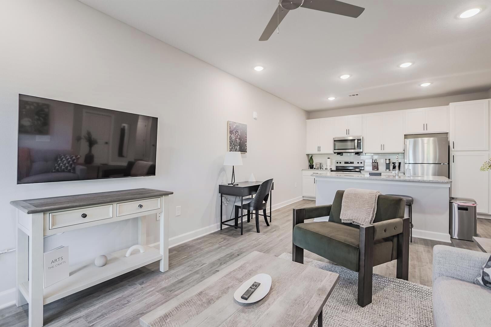 Una sala de estar moderna con un televisor de pantalla plana, un comedor con mesa y sillas, y una cocina con electrodomésticos de acero inoxidable.