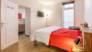 Un dormitorio con cama, televisor, lámpara y ventana.