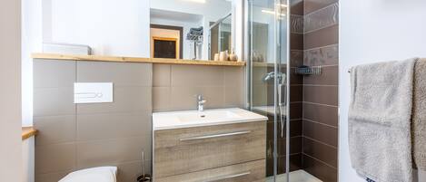 A modern bathroom with a glass shower enclosure, a white sink, and a wooden vanity.