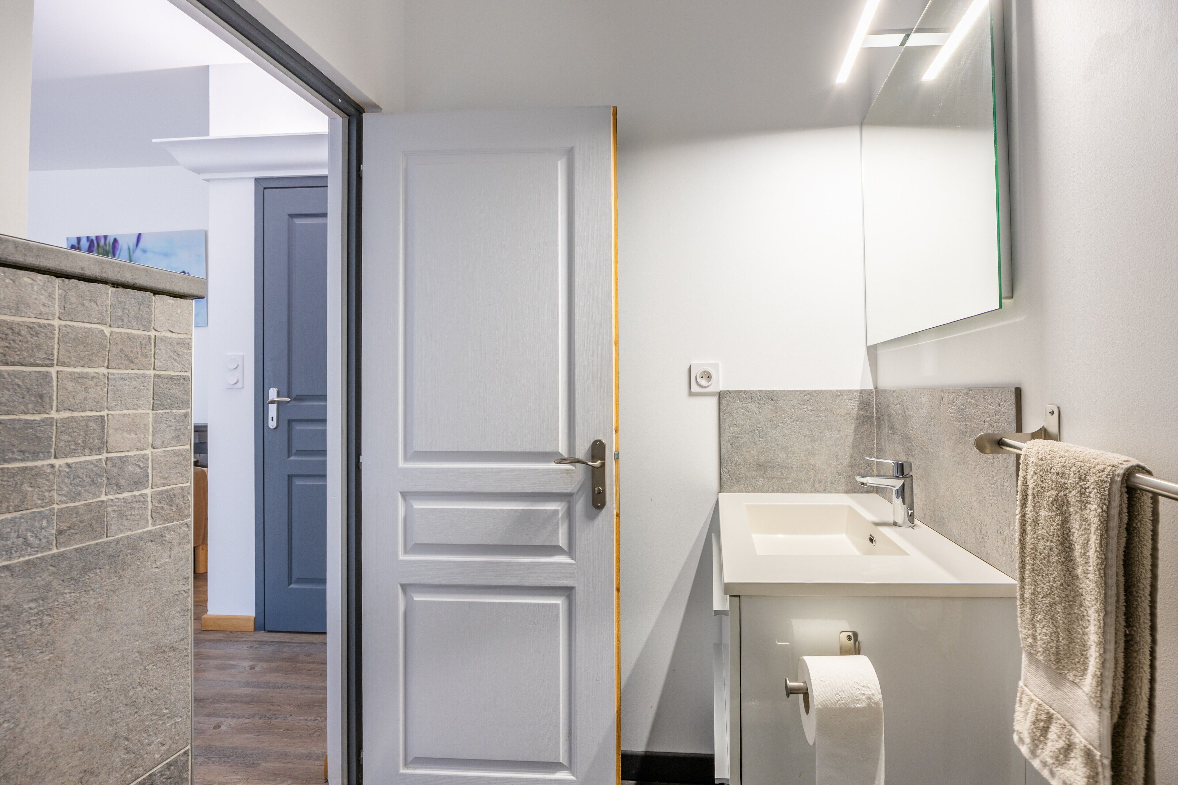 A bathroom with a white sink, a towel rack, and a door leading to another room.