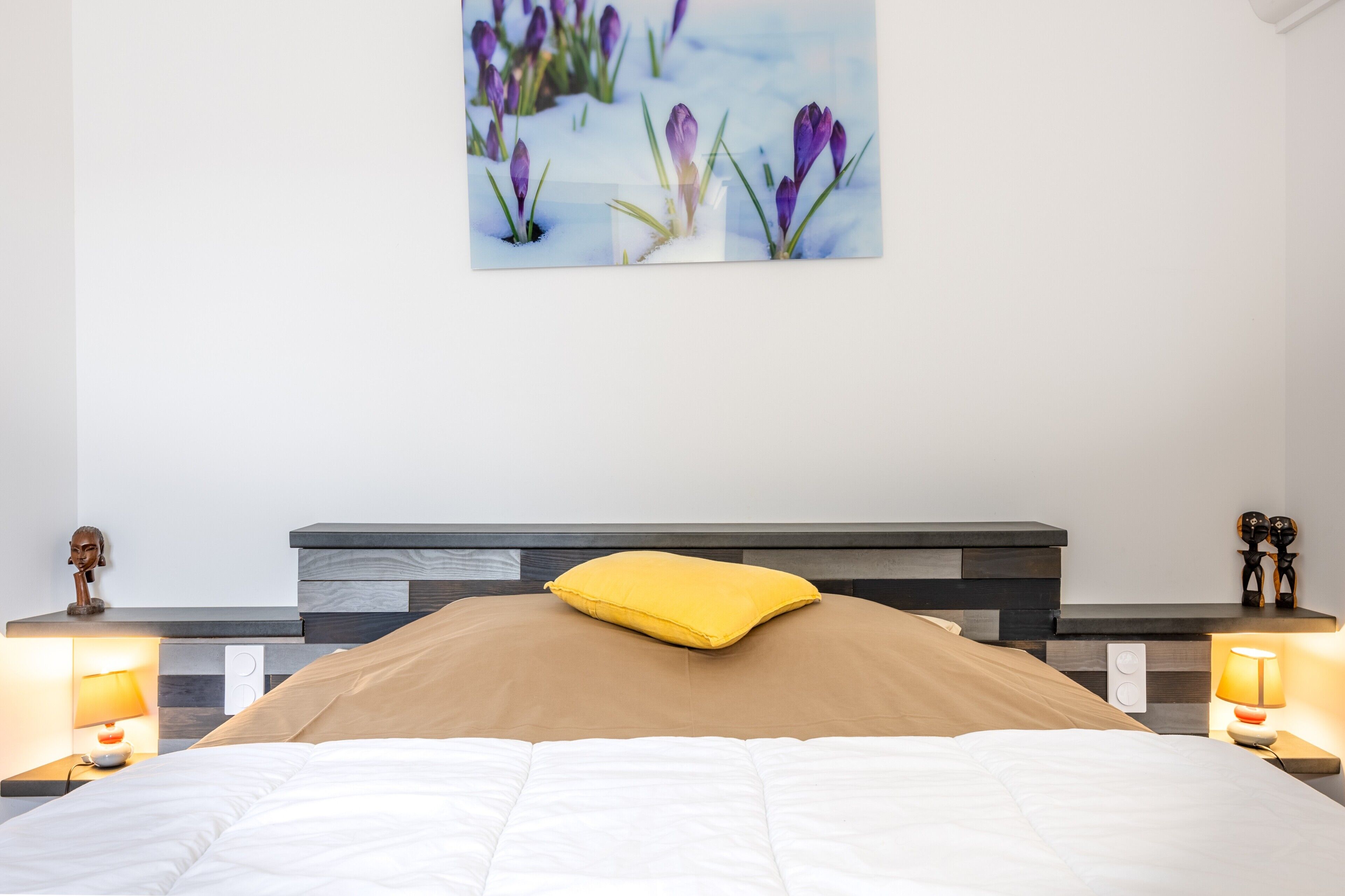 Een slaapkamer met een bed, nachtkastjes met lampen, een hoofdbord en een kunstwerk aan de muur.