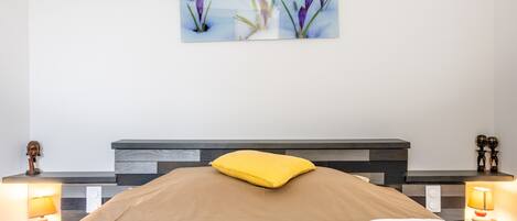 Une chambre à coucher comprenant un lit, des tables de chevet avec des lampes, une tête de lit et une œuvre d’art accrochée au mur.