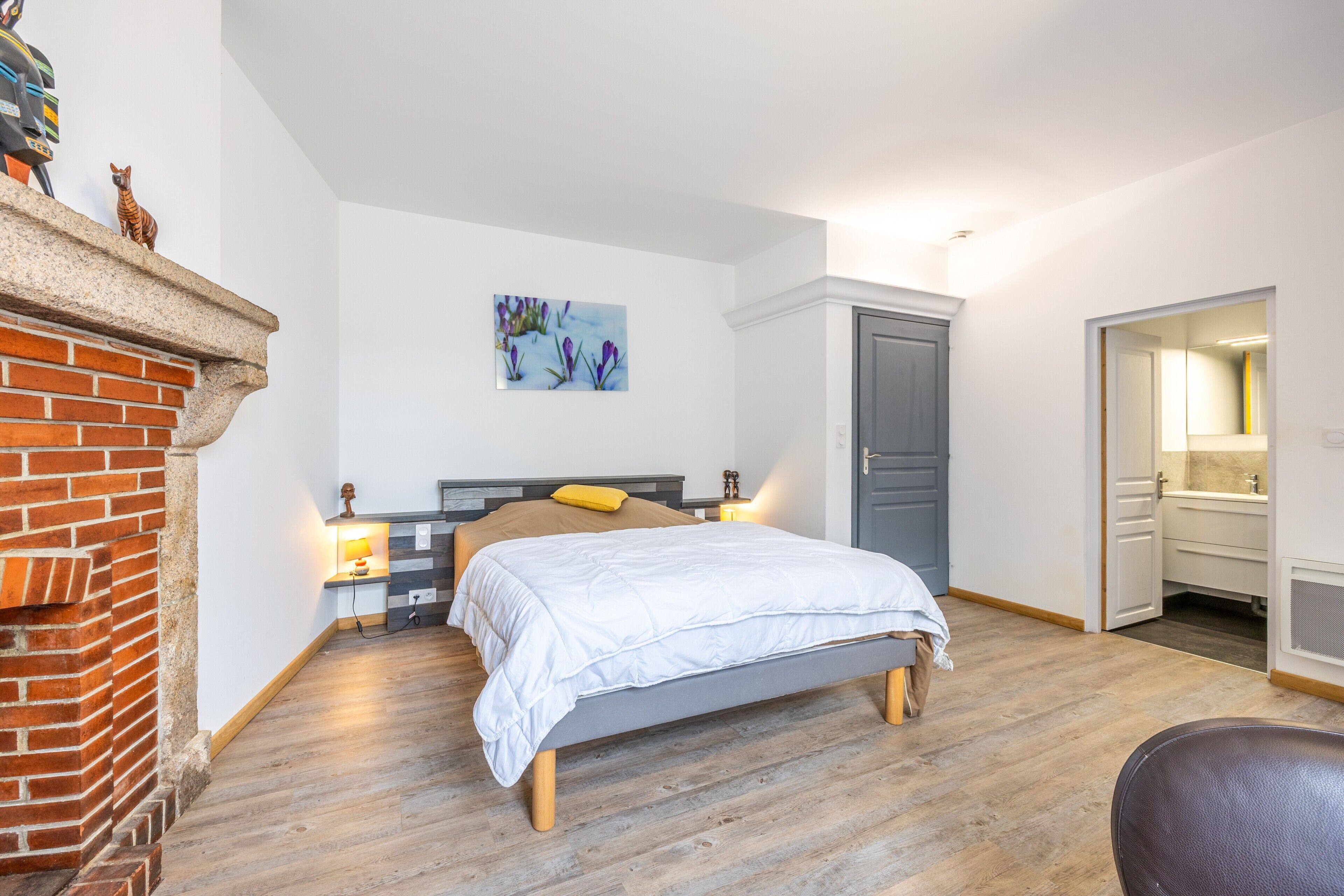 A bedroom with a bed, a fireplace, a painting, a wardrobe, and a bathroom.