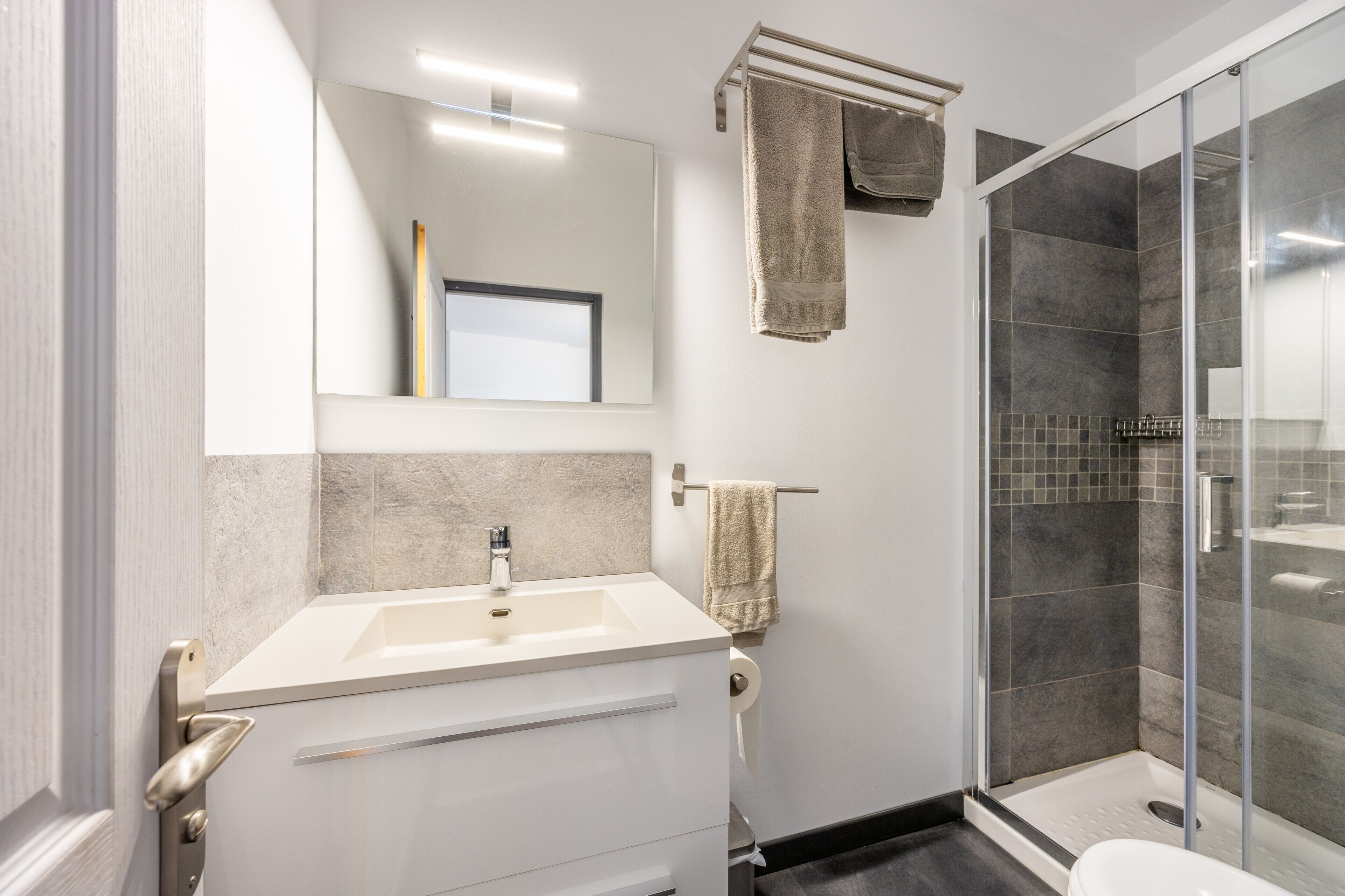 Un baño con lavamanos, espejo, toallero y cabina de ducha de vidrio.