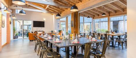 A spacious dining area with high ceilings and large windows, featuring multiple tables and chairs.
