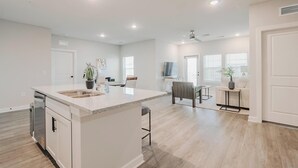 A spacious kitchen with a central island, a dining area with a table and chairs, and a living room with a sofa and a TV. - Landing | Stylish 2BD, Pool (Tice)