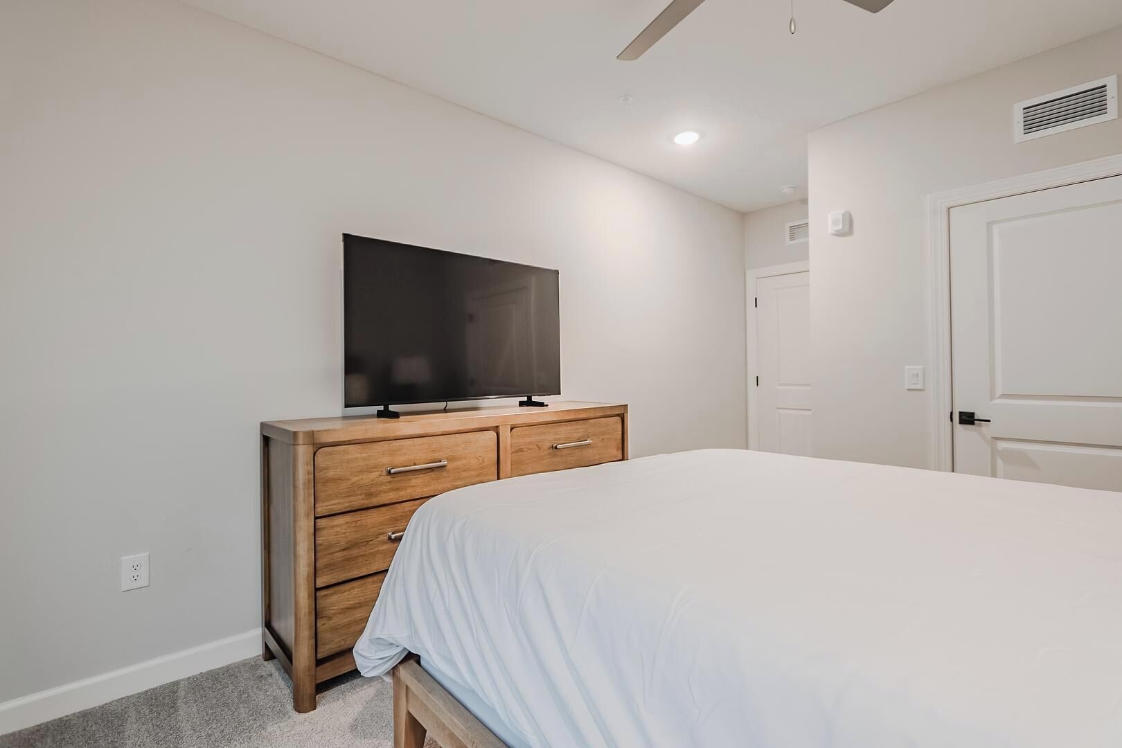 A bedroom with a bed, a wooden dresser, a television, and a door.