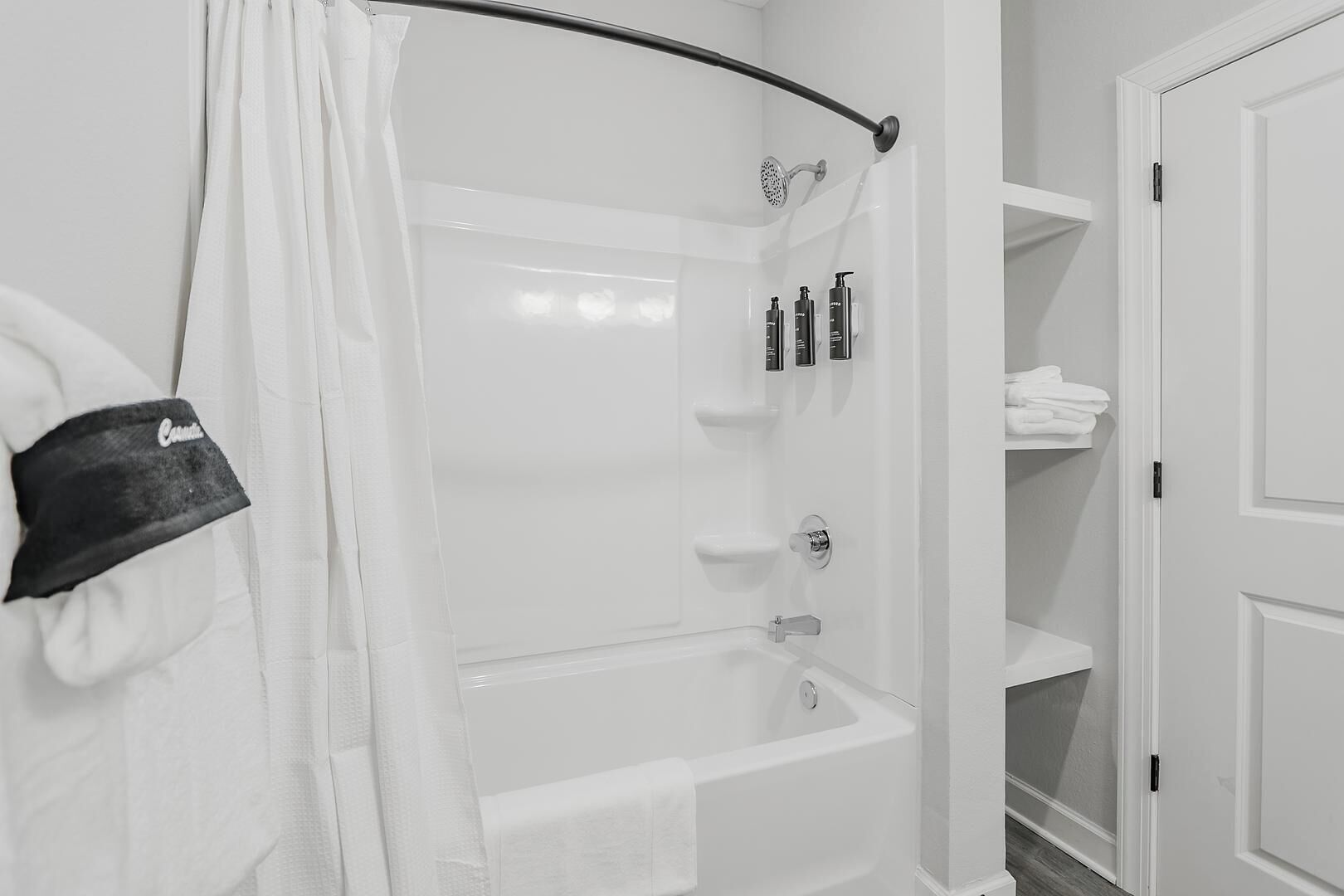 A bathroom with a bathtub, shower, and toilet. There are toiletries on the wall and a towel rack.